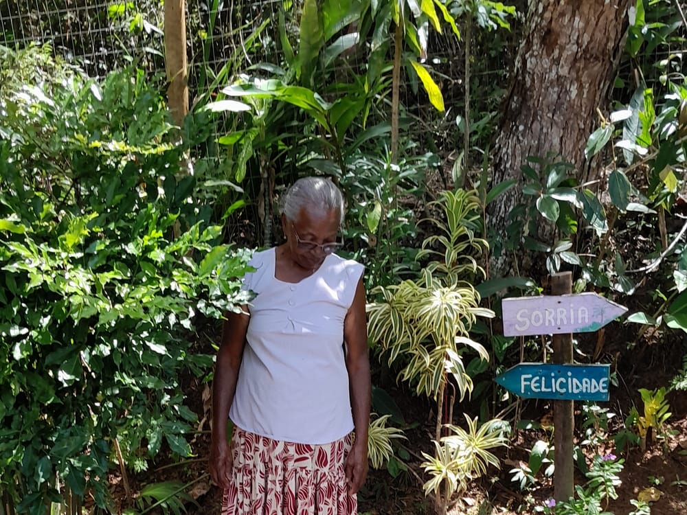Moradora do Quilombo Cachoeirinha no quintal, entre plantas e placas pintadas à mão