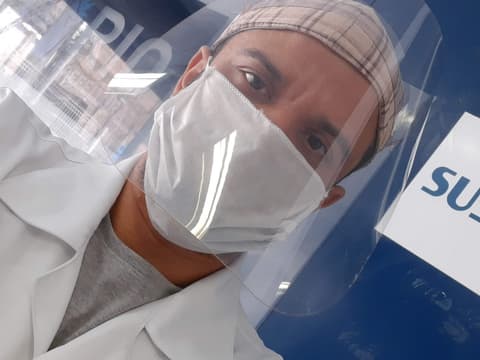 Atendimento no SUS com máscara e protetor facial, ao lado da placa do SUS